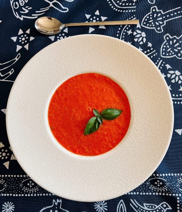 Bright red watermelon gazpacho served in a white bowl, garnished with fresh basil leaves.