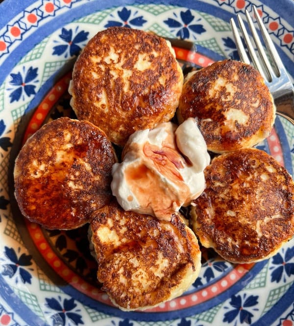 Golden brown syrniki topped with sour cream and jam.