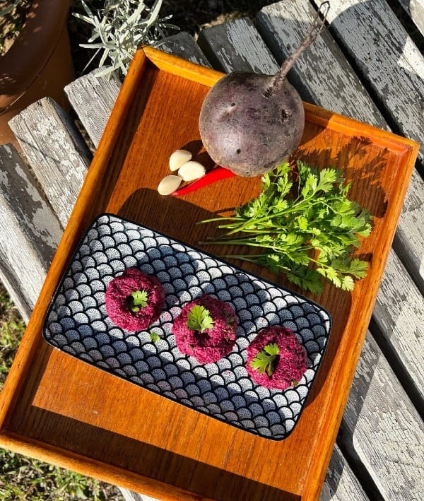 Vibrant beet pkhali balls garnished with cilantro, served on a blue plate.